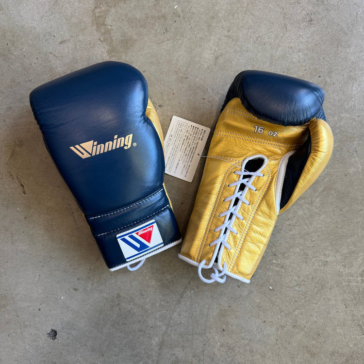 Blue and yellow boxing gloves on a concrete floor with a visible brand logo.